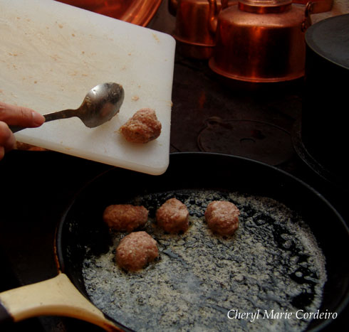 Gently rolling the meatballs into the frying pan with the help of a spoon