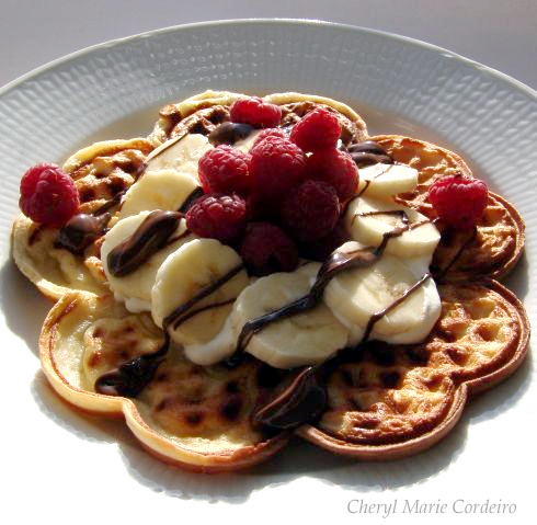 Homemade waffle topped with whipped cream, bananas, chocolate and raspberries